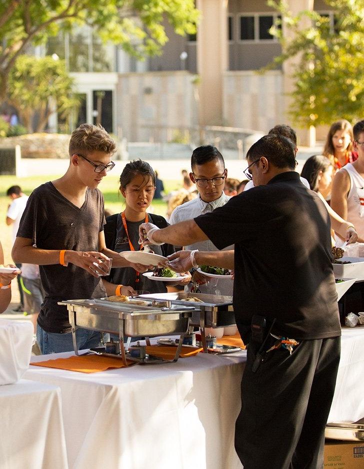 a server helps students at a catered buffet